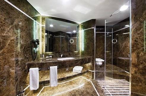 Ein elegantes Badezimmer im DoubleTree by Hilton Istanbul Esentepe Hotel mit Marmorwänden, einer Dusche und einem Waschbecken.