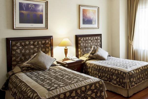Zwei Doppelbetten in einem Eresin Sultanahmet Hotelzimmer mit Nachttischen, Lampen und Gemälden an der Wand.