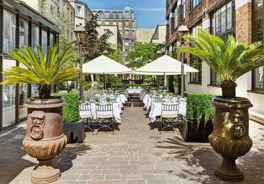 Außenbereich des Les Jardins du Marais Hotels mit Tischen, Stühlen und Sonnenschirmen.