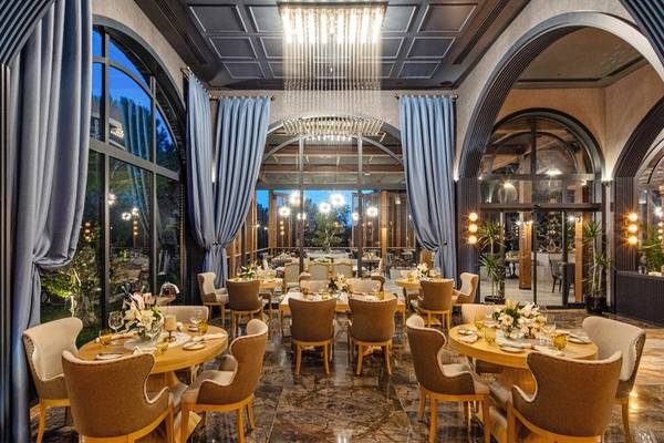 Innenansicht des Rixos Premium Belek Restaurants mit runden Tischen, Stühlen und Dekorationen.