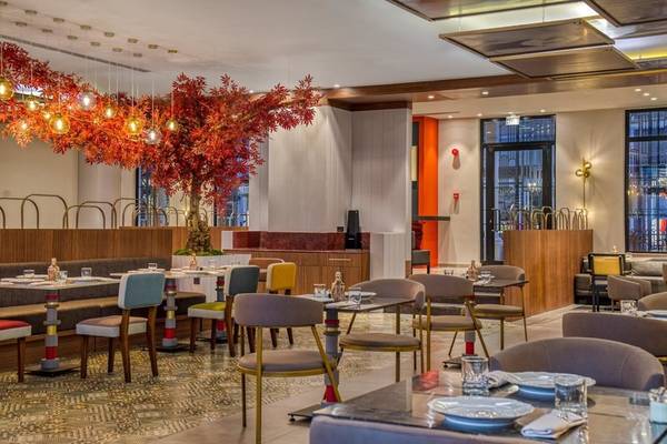 Innenansicht des Restaurants im Rixos Premium Belek mit bunten Stühlen und Tischen, einer roten Pflanze und moderner Einrichtung.