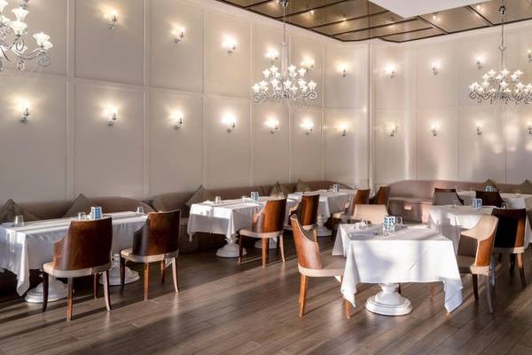Innenansicht des Rixos Premium Belek Restaurants mit weißen Tischen, Holzboden und Kronleuchtern.