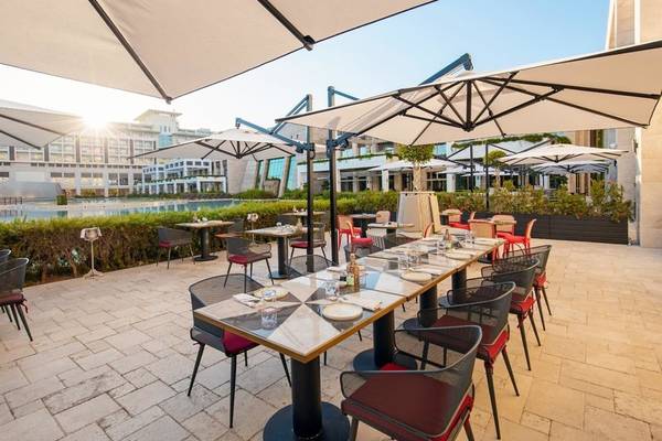 Terrasse des Rixos Premium Belek Hotels mit Tischen, Stühlen und Sonnenschirmen.