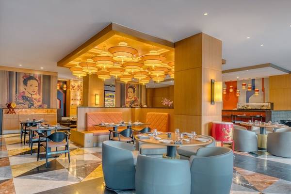 Innenansicht des Rixos Premium Belek Restaurants mit geometrischen Bodenfliesen, orangefarbenen Sofas und chinesischen Wandgemälden.