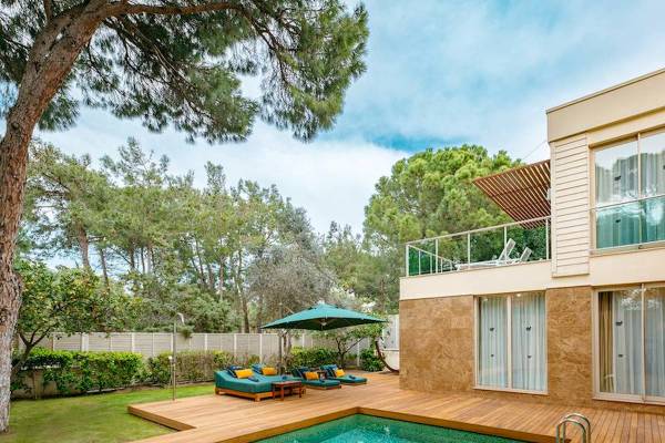 Poolseite der Rixos Premium Belek Villa mit Holzdeck, Loungesofas und einem grünen Sonnenschirm.