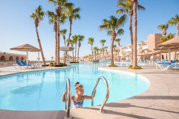 Ein kleines Mädchen klettert in den Pool des Pickalbatros Citadel Resorts, umgeben von Palmen und Sonnenliegen.