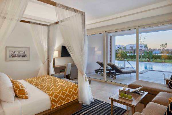 Schlafzimmer im Steigenberger Resort Alaya mit Baldachin-Bett, Swimmingpool und Terrasse im Hintergrund.