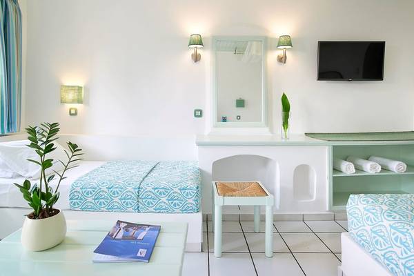 Innenansicht eines Zimmers im Mitsis Cretan Village Hotel mit zwei Betten, einem Fernseher und einem Tisch.