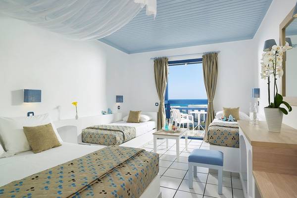 Innenansicht eines Zimmers im Mitsis Cretan Village Hotel mit drei Betten, Balkon und Meerblick.