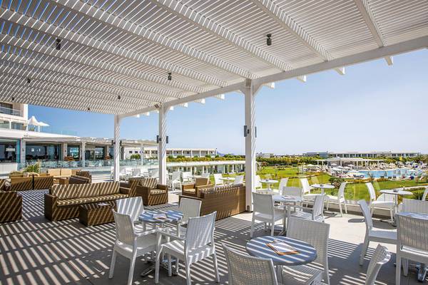 Terrasse im Asterias Beach Resort mit weißen Möbeln und Sonnenschutz.