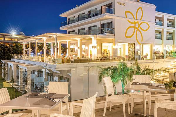 Nachtansicht des Asterias Beach Resort Sentido mit Außenterrasse, beleuchteten Tischen und Stühlen.