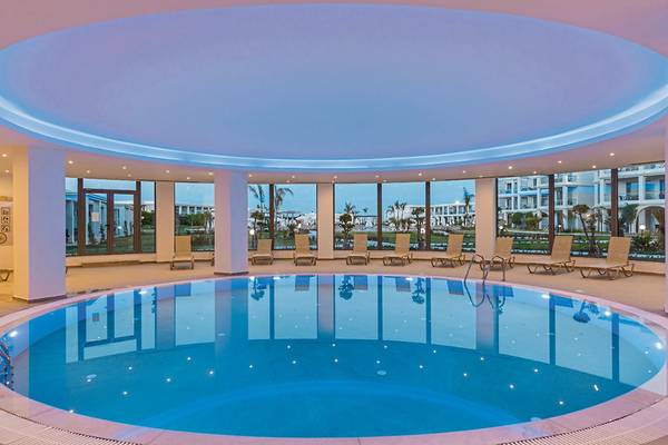 Innenpool des Asterias Beach Resorts mit Lounge-Sesseln und Glaswänden.