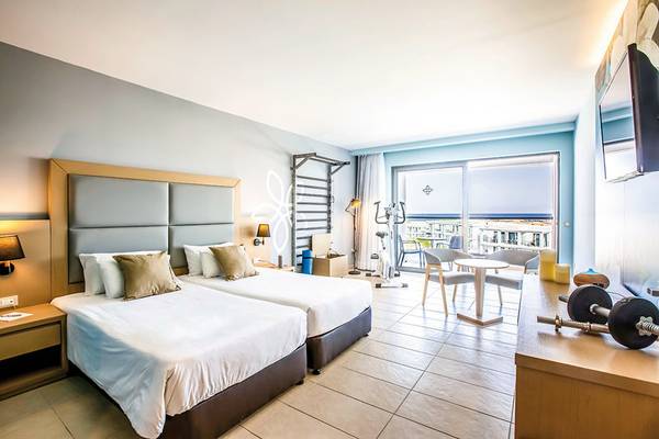 Innenansicht eines Doppelzimmers im Asterias Beach Resort mit zwei Betten, Schreibtisch und Fitnessgeräten.