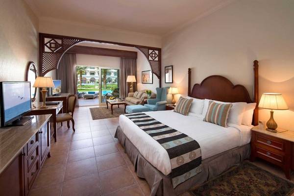 Schlafzimmer im Baron Palace Sahl Hasheesh Hotel mit einem großen Bett, Fernseher, Nachttischen und Lampen.