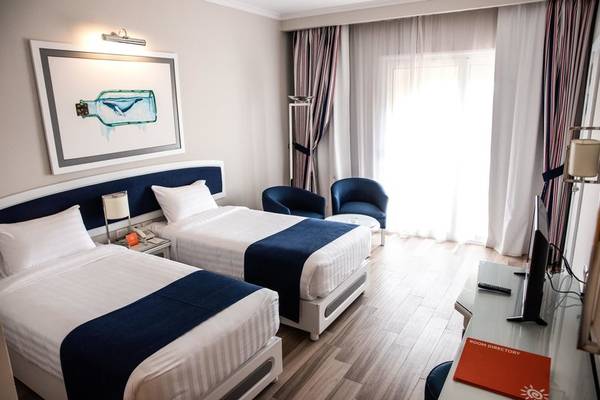 Doppelzimmer im Desert Rose Resort mit zwei Betten, Nachttischen, Lampen und einem Fenster mit Vorhängen.