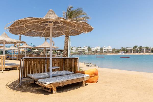 Strand des Desert Rose Resorts mit Sonnenliegen und Strohschirmen