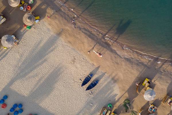 Luftaufnahme des Desert Rose Resorts Strands mit mehreren Liegen, Sonnenschirmen und blauen Booten im Sand.