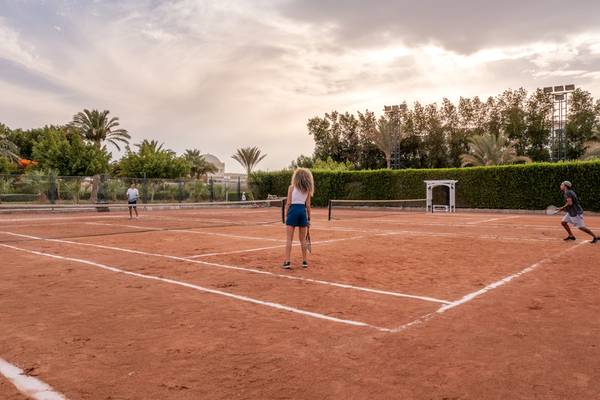 Tennisplatz im Hotel Desert Rose Resort mit drei Spielern und einer Person, die in der Mitte steht.