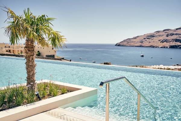 Außenpool des Lindos Grand Resort & Spa mit Blick auf das Meer und eine Palme.