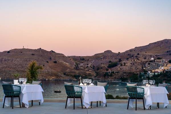 Außenbereich des Lindos Grand Resort & Spa mit gedeckten Tischen und Blick auf die Berge und den See.
