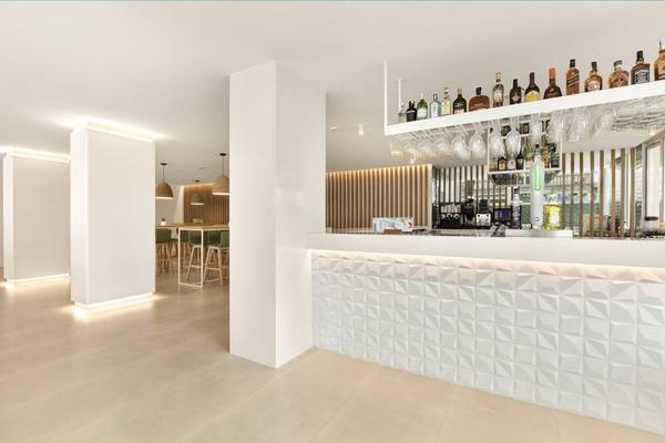 Innenansicht der Bar im THB Gran Playa Hotel mit weißen Wänden, geometrischen Mustern und einer Theke mit Flaschen.