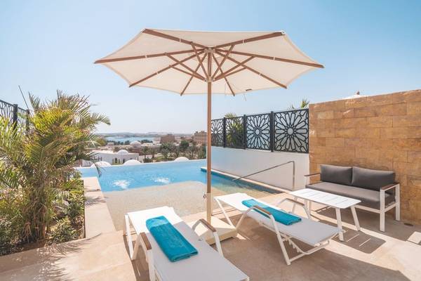 Außenbereich des Fort Arabesque Resorts mit Swimmingpool, Sonnenliegen und Sonnenschirm.