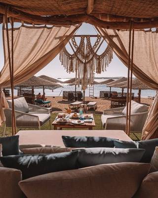 Loungebereich am Strand im Fort Arabesque Resort, Spa & Villas mit Tischen, Stühlen und Sonnenschirmen.