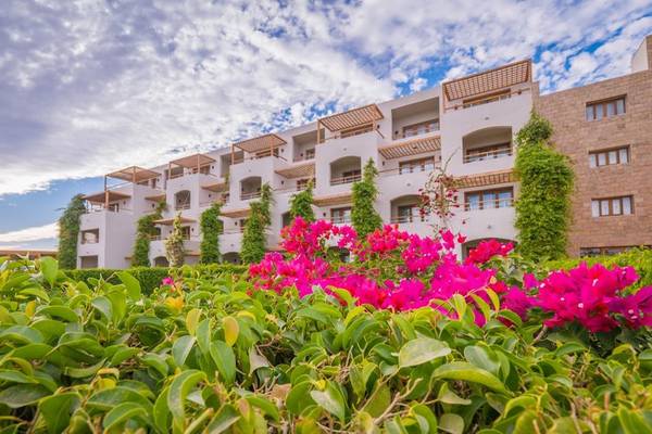 Außenansicht des Fort Arabesque Resorts mit rosa Bougainvillea vor dem Gebäude.