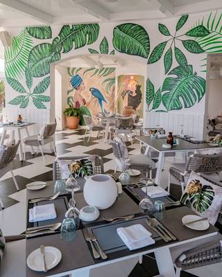 Innenbereich des Restaurants im Fort Arabesque Resort, Spa & Villas mit grünen Blattmalereien an den Wänden und einem schwarzen und weißen Schachbrettboden.