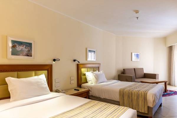 Schlafzimmer im Fort Arabesque Resort mit zwei Betten, Couch, Nachttischen und Gemälden.