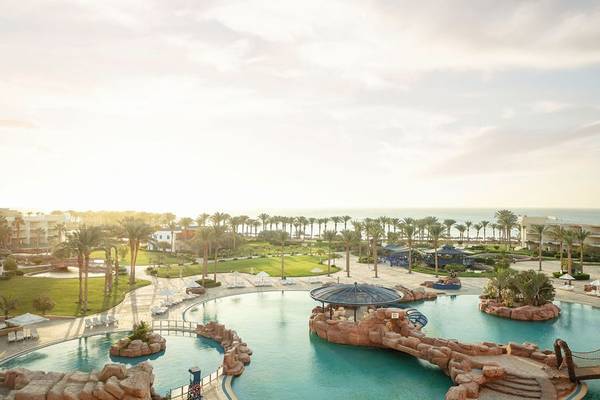 Außenansicht des Palm Royale Soma Bay Resorts mit Swimmingpool, Sonnenliegen und Palmen.