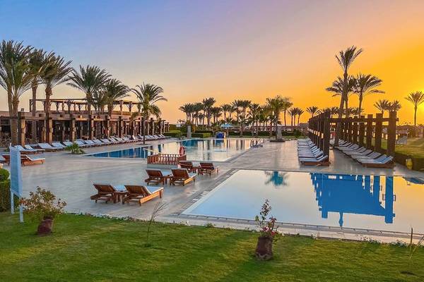 Gemma Resort Poolbereich bei Sonnenuntergang mit Sonnenliegen, Palmen und Gebäuden