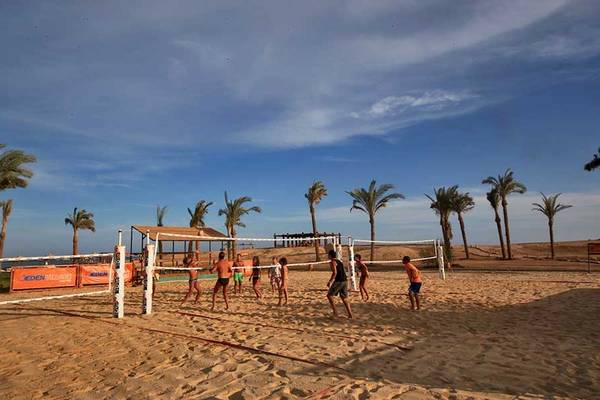 Mehrere Personen spielen Volleyball auf einem Sandplatz mit Palmen im Hintergrund im Gemma Resort.