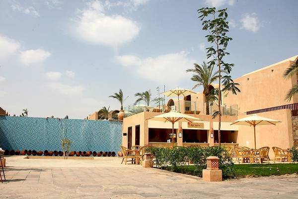 Außenbereich des Gemma Resorts mit blauer Wand, Sonnenschirmen und Tischen.