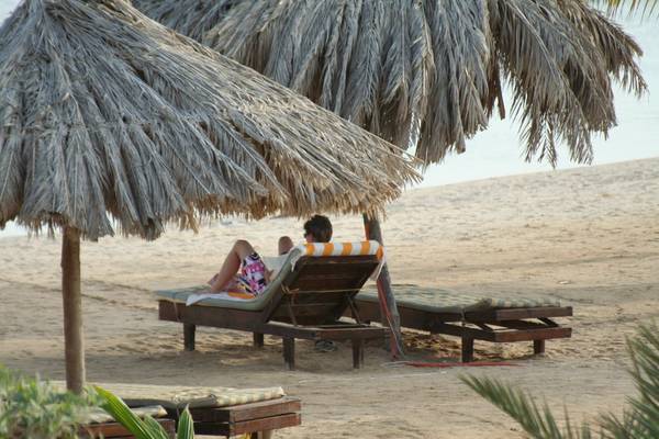 Person auf Liegestuhl unter Strandhut am Strand von Mangrove Bay Resort