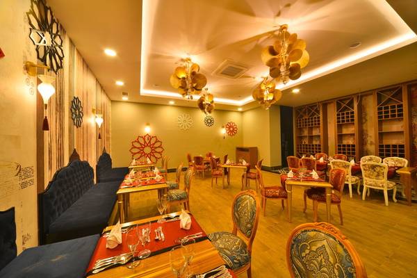 Innenbereich eines Restaurants im Seaden Valentine Resort & Spa mit runden Tischen, Stühlen und dekorativen Kronleuchtern.
