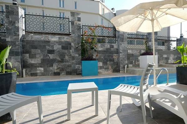 Poolbereich des Seaden Valentine Resort & Spa mit weißen Liegestühlen, einem Tisch und einem Schirm.