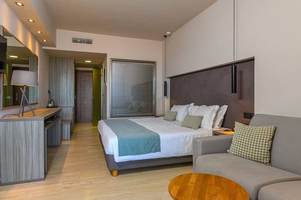 Ein modernes Hotelzimmer im Alexandra Beach Resort mit einem großen Bett, Sofa, Schreibtisch und vielen Fenstern.