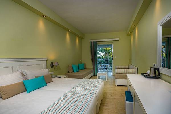 Innenansicht eines Hotelzimmers im Alexandra Beach Resort mit Doppelbett, Sofa und Balkon.
