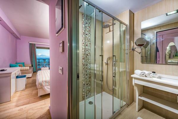 Das Badezimmer im Alexandra Beach Resort mit rosa Wand, Glasdusche und Spiegel.