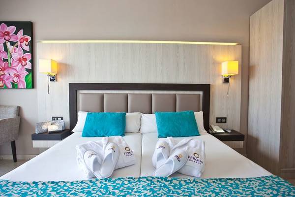 Doppelbett im Hotelzimmer von Fergus Style Bahamas mit blauen Kissen und weißen Handtüchern