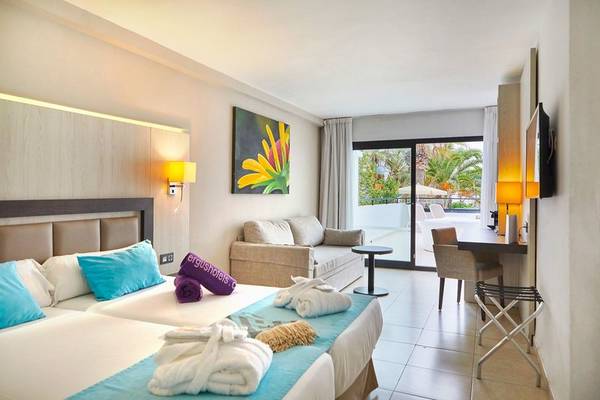 Ein modernes Hotelzimmer im Fergus Style Bahamas Hotel mit zwei Betten, Kissen und Decken, einem Sofa und einem Tisch.