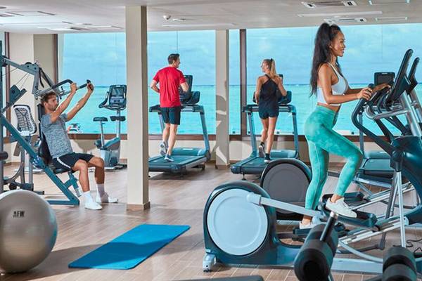 Fitnesscenter im RIU Atoll Hotel mit Mitgliedern, die auf Geräten trainieren und einen Blick auf das Meer genießen.