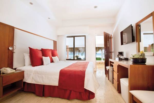 Ein modernes Hotelzimmer mit einem großen Bett, roten Kissen, einer offenen Tür und einem Blick auf den Strand.