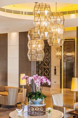 Lobby-Lounge des Barcelo Mussanah Resorts mit großen Leuchten und rosa Orchideen.