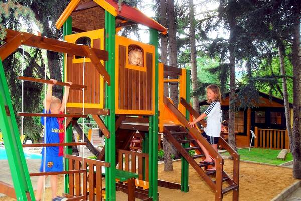 Ein Kinderspielplatz mit einer Rutsche und Klettergerüst im Wald mit drei Kindern, die spielen.