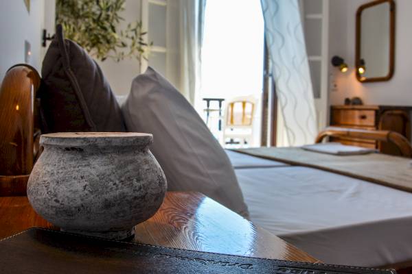Doppelbett im Schlafzimmer des Sunrise Hotels Samos mit grauen Kissen und einer Vase auf dem Tisch.