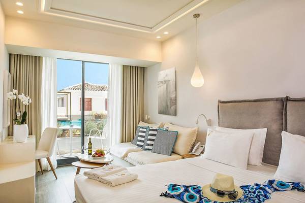 Schlafzimmer im Samian Mare Hotel Suites & Spa mit Doppelbett, Sofa, Tisch und Aussicht auf den Pool.