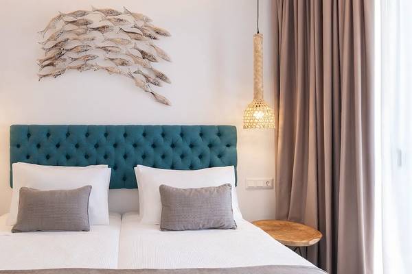 Schlafzimmer im Kalidon Panorama Hotel mit blauem Kopfteil, weißen Kissen und hängenden Lampen.