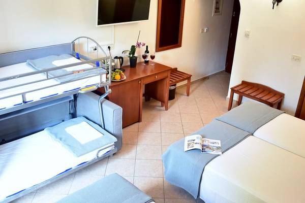 Hotelzimmer mit zwei Doppelbetten, einem Schlafsofa, einem Fernseher und einem Tisch mit Früchten und Weingläsern.
